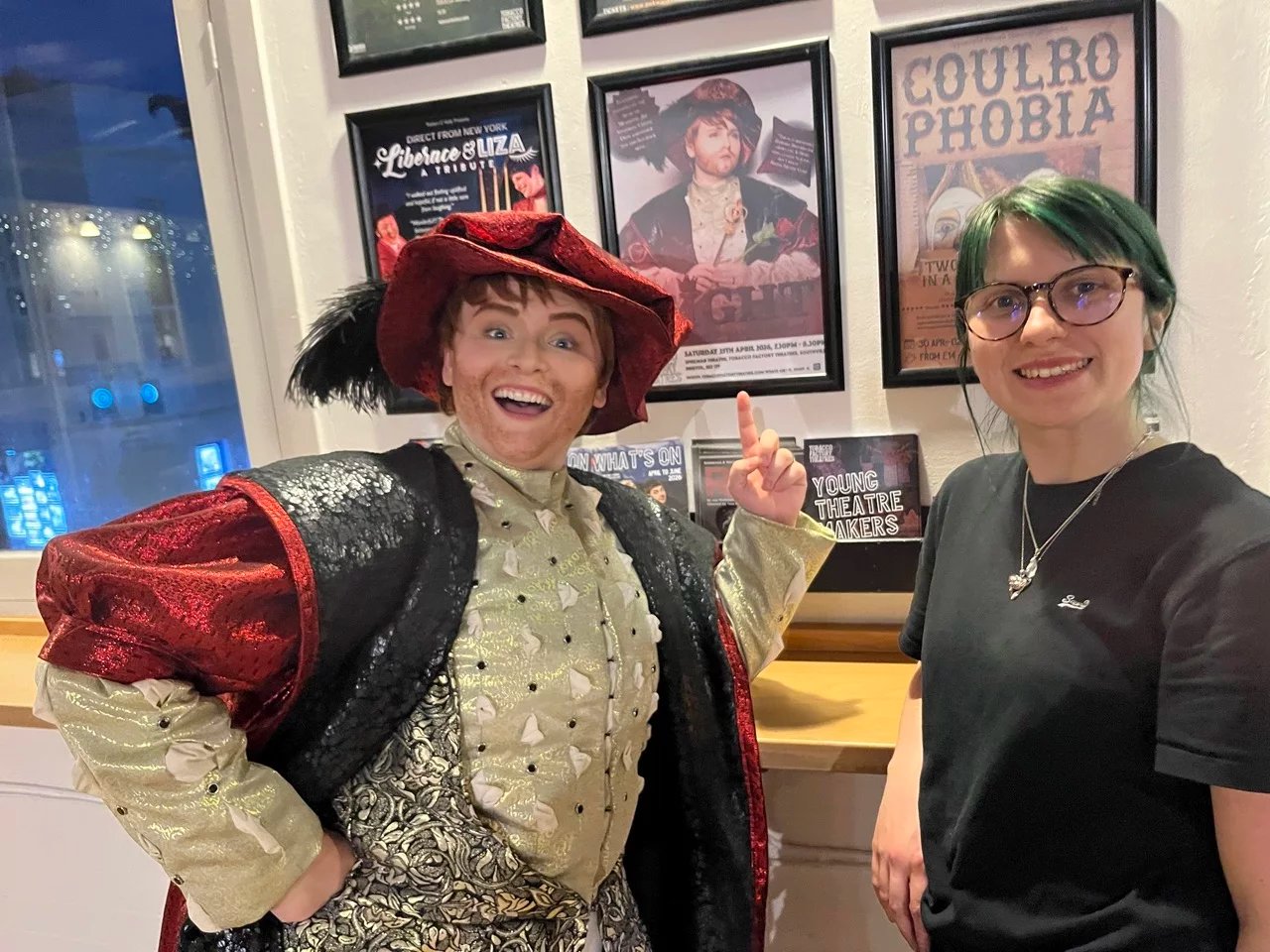 A selfie with Billie-Jo Rainbird standing on the right and Hannah Clift in drag as Henry the eighth on the left. Hannah is pointing at a poster of her show Eight.